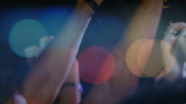 Audience responding to music beat, raising and clapping with yellow band and glasses over bokeh