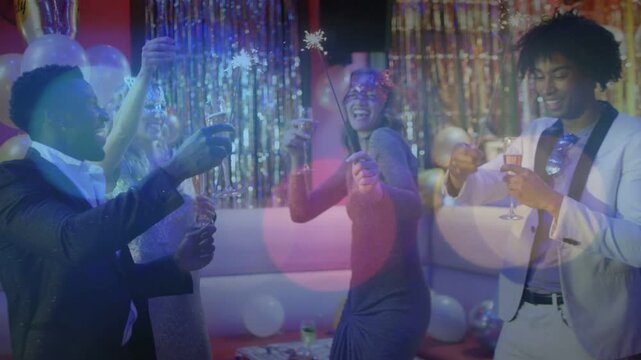 Group of four party guests raising glasses and waving sparkler, celebrating with sparks drifting
