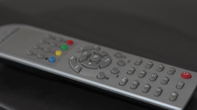 Silver television remote control with colorful buttons on dark surface