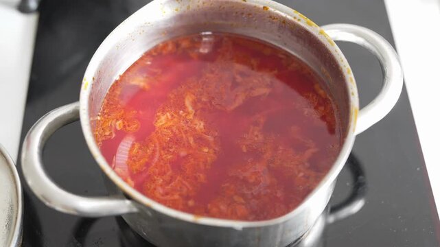 Red soup cooking in a metal pot on electric stove