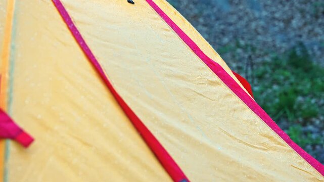 Raindrops sliding on waterproof yellow tent fabric in close-up during outdoor camping in forest, showing water repellent textile texture.