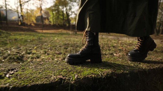 Stylish Woman Walks In Leather Boots By Concrete Parapet In Autumn Park