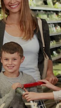 Vertical video: Grabbing red bar, mom pushing kids through grocery aisle, pineapple and data rising