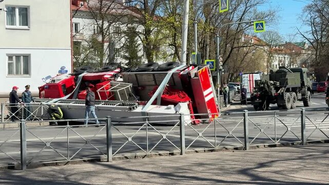 Kaliningrad Russia April 18 2026: Responders and a heavy recovery vehicle stand beside an overturned fire truck at an accident site on a city street.