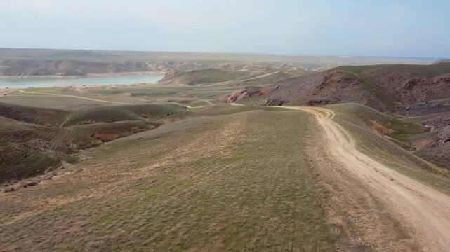Aerial drone flight over spring steppe with dirt road and Kurty Reservoir, Kazakhstan landscape