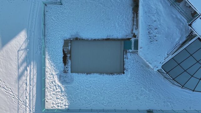 Aerial view of a modern building with a distinct glass roof and swimming pool surrounded by snow. Birds Eye View