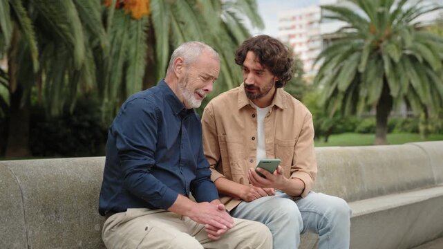 Young man using smartphone to share content on social media, with senior man. Family bonding with digital technology