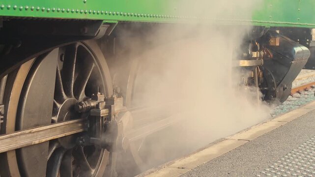 A steam train arrives at a historic railway station in France. Smoke billows as the wheels turn, showcasing vintage railway infrastructure in a daytime setting.