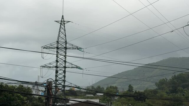 Metal electricity pylons and suspended power lines extend across hilly terrain beneath an overcast sky forming part of a large regional energy network. Power transmission.