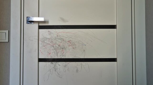 Child drawing with crayons on a white interior door, messy scribbles on wall surface. Concept of kids creativity, naughty behavior, home damage, and parenting challenges.