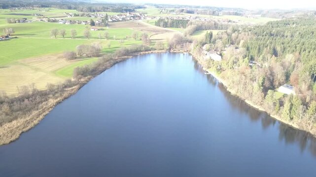 Aerial landscape featuring lake, forest and open fields near mountain range in southern Germany.