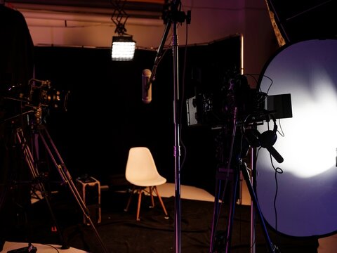 Warm lights illuminate a sleek podcast studio filled with cameras and microphones, creating an inviting space for engaging interviews. The empty white chair awaits its guest, inspiring anticipation