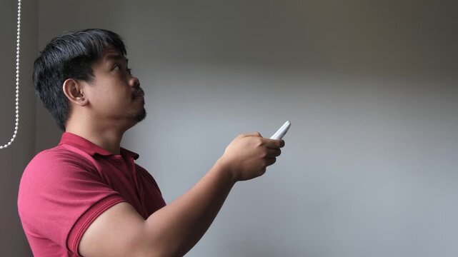 Southeast Asian man turning on the air conditioner by remote AC indoor