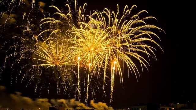 Bright golden fireworks exploding in the night sky over city buildings during celebration event