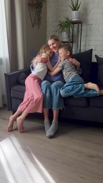 Two kids runs and hug mother on comfortable couch at home living room, happy laughing mom with adorable loving daughter and son. Mothers day, birthday celebration