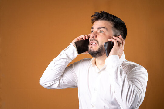 Hombre de oficina sosteniendo dos tel&eacute;fonos y con cara de abrumado. Concepto de estres laborar y sobre comunicaciones