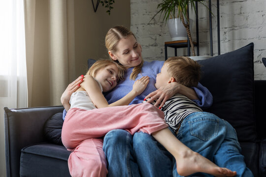 Mother with two kids embracing on cozy couch at home living room. Mom with adorable loving daughter and son spending time together. Family bonding, trust un support