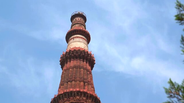 A static low-angle shot of the Qutb Minar, the world's tallest brick minaret, showcasing its intricate red sandstone carvings and marble sections against a clear blue sky in New Delhi.