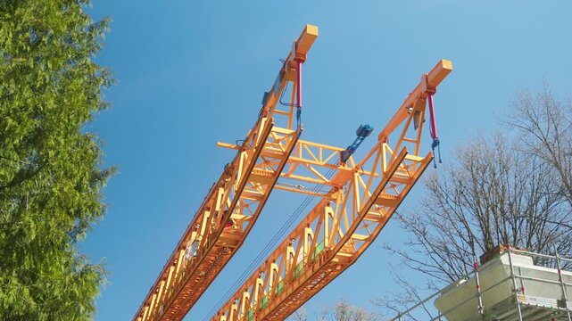 Handheld perspective looks up at the yellow steel truss tip of a massive segment launcher machinery extending into the clear blue sky over the Fraser Highway during construction of the Surrey Langley