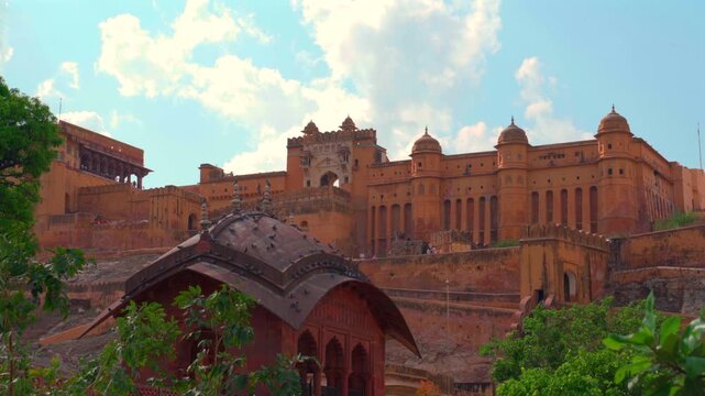 A static wide shot of the majestic Amber Fort (Amer Fort) in Jaipur, showcasing its massive sandstone walls, ornate pavilions, and the main Sun Gate (Suraj Pol) against a bright blue sky.