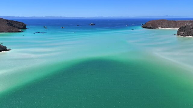4K aerial view of Playa Balandra in La Paz, showing calm clear water with yachts in the distance on a bright sunny day.