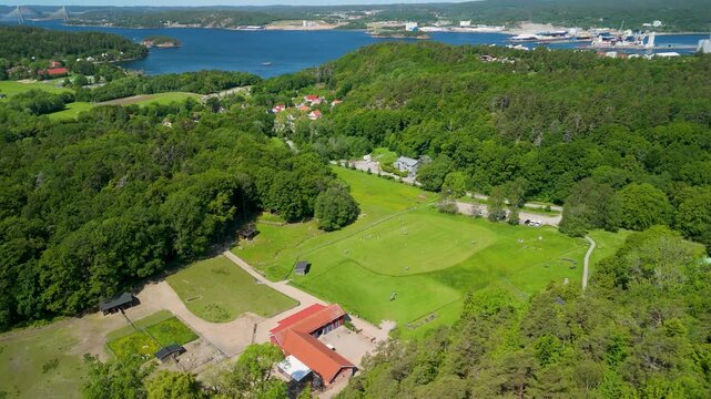 Aerial drone parallax shot over Emaus farm estate in Uddevalla Sweden with green meadows, red-roof buildings, fjord and suspension bridge