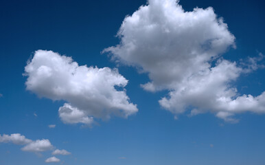 Fototapeta premium Partly cloudy sky with three cloud formations of different sizes against a smooth gradient from dark blue at the top to lighter blue at the bottom