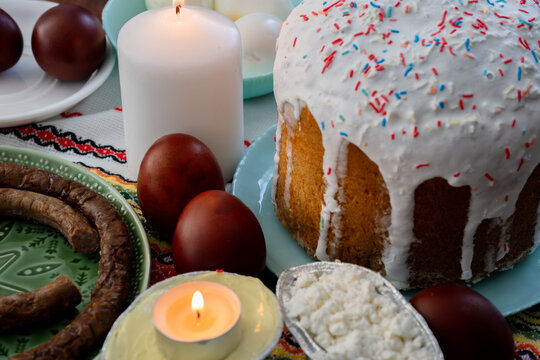 a traditional ukrainian easter table setting featuring a tall homemade paska bread topped with white icing and colorful sprinkles, surrounded by naturally dyed brown krashanky eggs