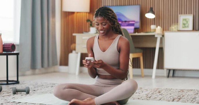 Black woman, phone and texting with exercise in home on yoga mat, break and happy with funny post on web. African person, smartphone and rest for fitness on floor, mobile app or social media at house