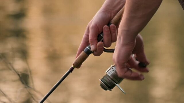 Close up of fisherman hands reeling fishing line with spinning rod. Outdoor leisure activity, angling, hobby and nature lifestyle concept. High quality FullHD footage