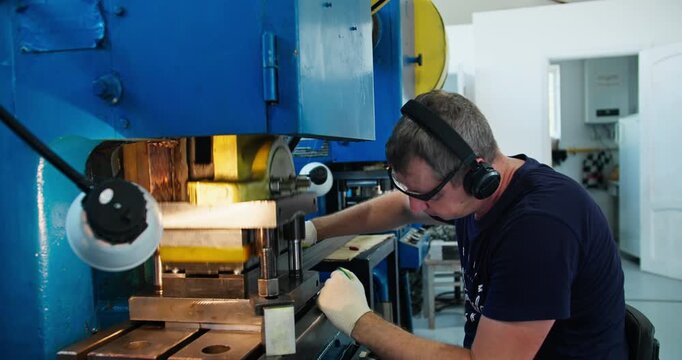 Blue collar worker at metal stamping machine in factory. Industrial production and skilled manual operation