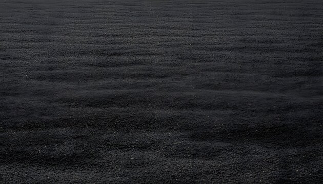 Close-up view of a dark, textured surface resembling black sand or volcanic ash with subtle ripples extending across the frame.