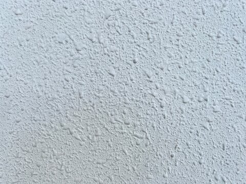 Full frame background of a white stucco popcorn texture finish on a ceiling or wall surface.