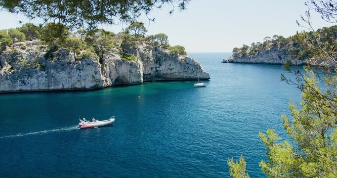 Coastal landscape of Calanque de Port-Miou with cruising boat, steep limestone cliffs, calm Mediterranean sea under bright daylight