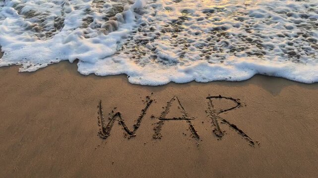 Ocean wave erasing word war written on sandy beach at sunset