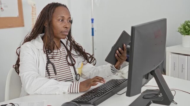 Woman doctor with stethoscope holds tablet and types on keyboard at desk in building medical clinic; medical efficiency concentration.