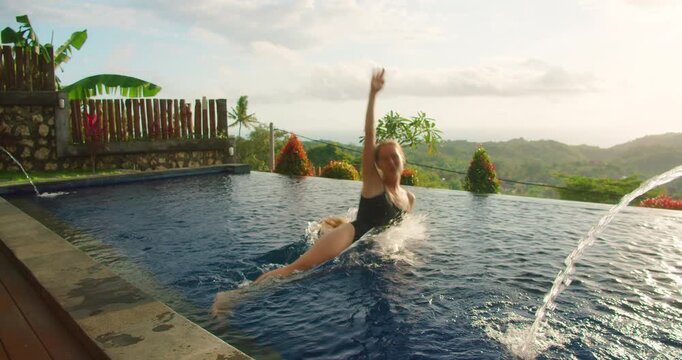 Woman splashes into infinity pool at tropical villa with hills during sunrise capturing joy and luxury resort lifestyle