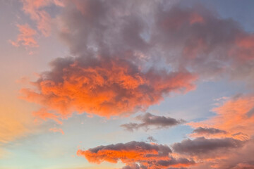 Fototapeta premium Dramatic sunset clouds with vibrant orange and red tones against soft blue sky. Atmospheric natural background with dynamic cloud formations, mood, weather, scenic concepts