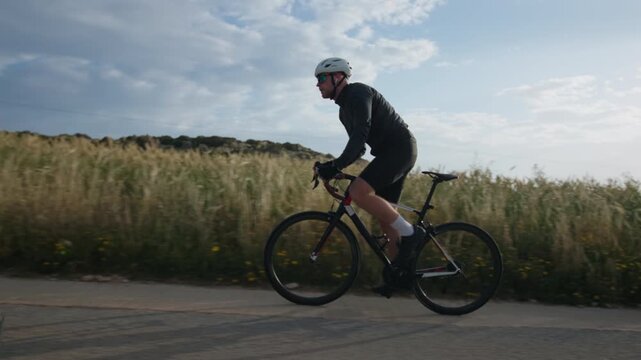 Athletic male cyclist wearing helmet riding bike on scenic road pedaling during outdoor training cardio exercise fitness routine and healthy lifestyle concept