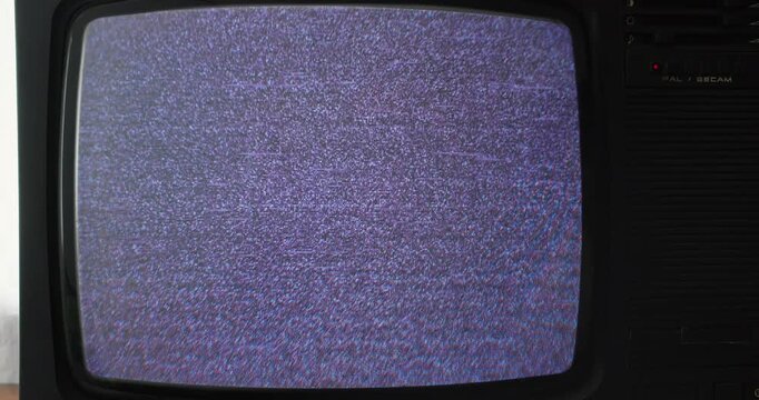 Analog television powering on from a dark screen to visible TV static. Vintage broadcast equipment and obsolete home entertainment technology