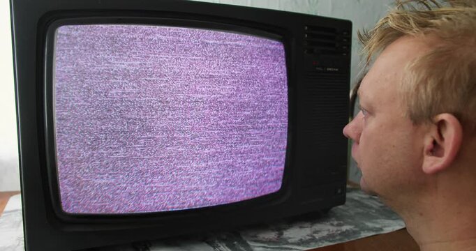 Man looking CRT television displaying TV static. Screen hypnosis and mindless viewing