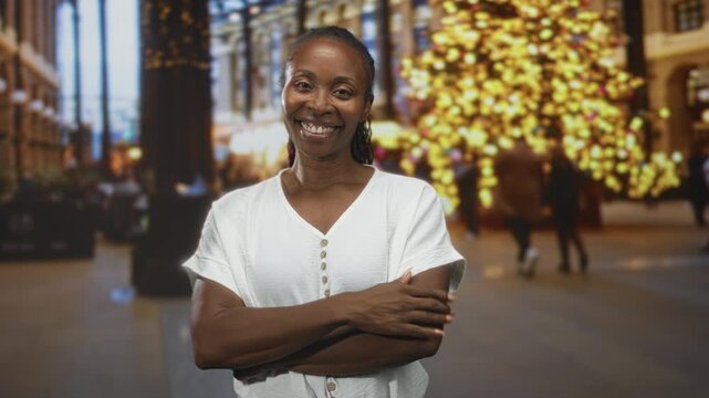 Young woman smiling with arms crossed and hand to chest in a building mall atrium with christmas tree and lights; warm gratitude.