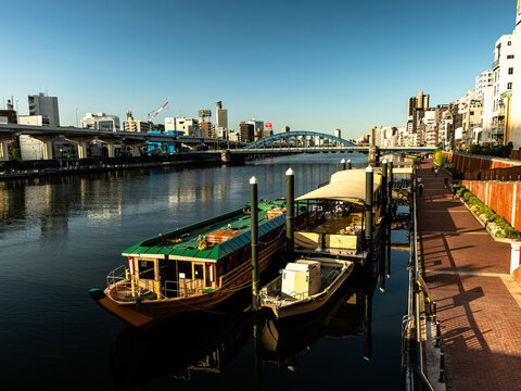Traditional Yakatabune houseboats moored on the Sumida River at golden hour, contrasting with the modern Tokyo city skyline