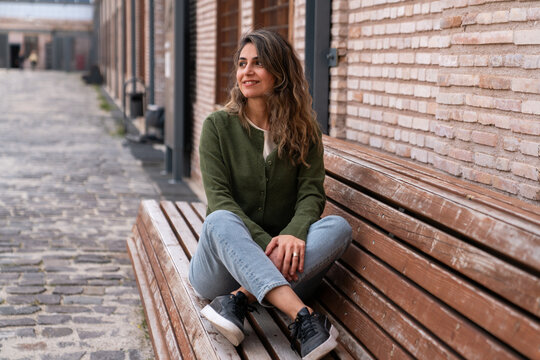 Young Woman Sitting on Wooden Bench in Urban Street Casual Lifestyle Portrait Looking Away