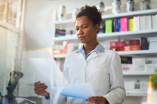 Black female pharmacist reading list of medicine while working in pharmacy