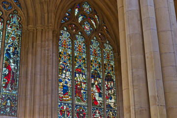 Vibrant stained glass windows illuminate an old stone church interior, depicting figures and patterns within grand arches and pillars in Beverley Minster - Yorkshire - Great Britain © Robert