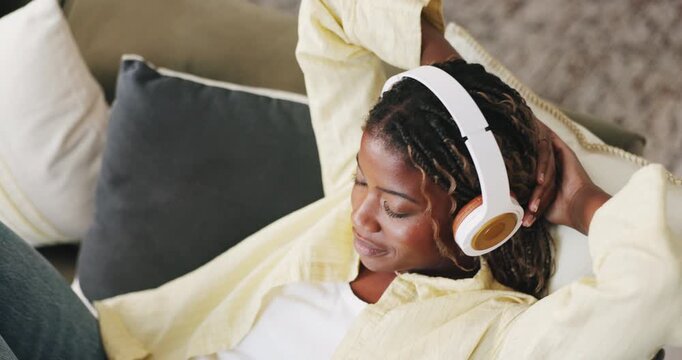 Relax, stretching and black woman with headphones on sofa, audiobook chapter and calming lofi track. Chill, mindfulness podcast and happy person with tech for streaming music, above and peace in home