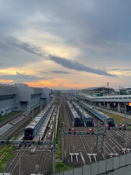 A wide-angle view of a railway depot at sunset shows multiple blue trains aligned on parallel tracks stretching into the distance.