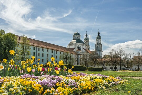 St. Lorenz Basilica and Residenz in Kempten, Allgau, Germany. Scenic view with spring flowers in the Hofgarten park under a blue sky. Historic Bavarian landmark and famous pilgrimage church.