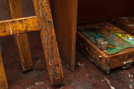 An old palette with oil paints in the artist's studio next to an easel on the floor. Photo hobby for creative people. 